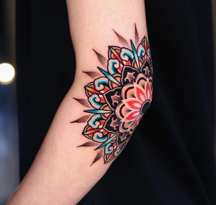 Colorful mandala elbow tattoo design on forearm, featuring intricate geometric patterns with vibrant hues.