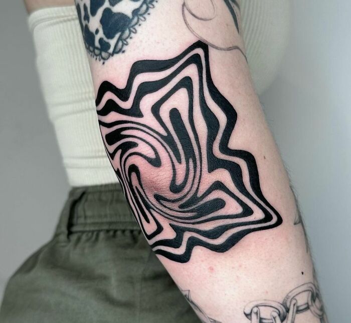 Abstract black pattern elbow tattoo on a person's arm with additional tattoos in view.