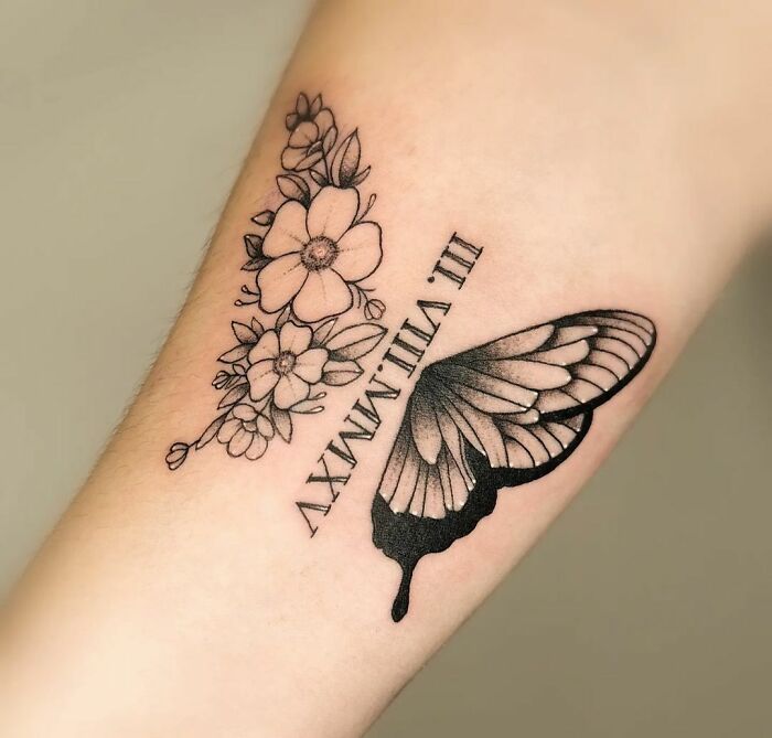 Butterfly and flowers memorial tattoo with a date in Roman numerals to honor family.