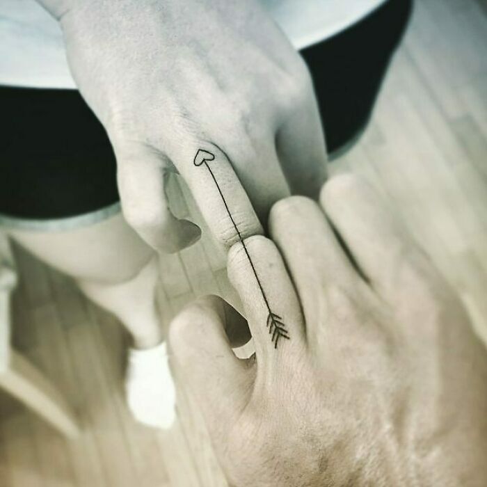 Minimalistic family tattoo with arrow design symbolizing unbreakable bonds on intertwined fingers.