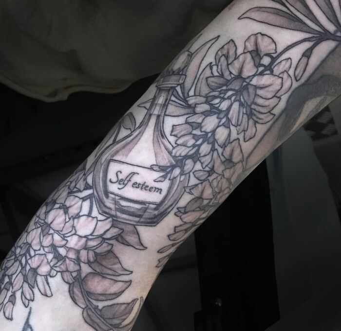 Arm tattoo featuring a bottle labeled "self esteem" with floral designs, symbolizing self-love and empowerment.