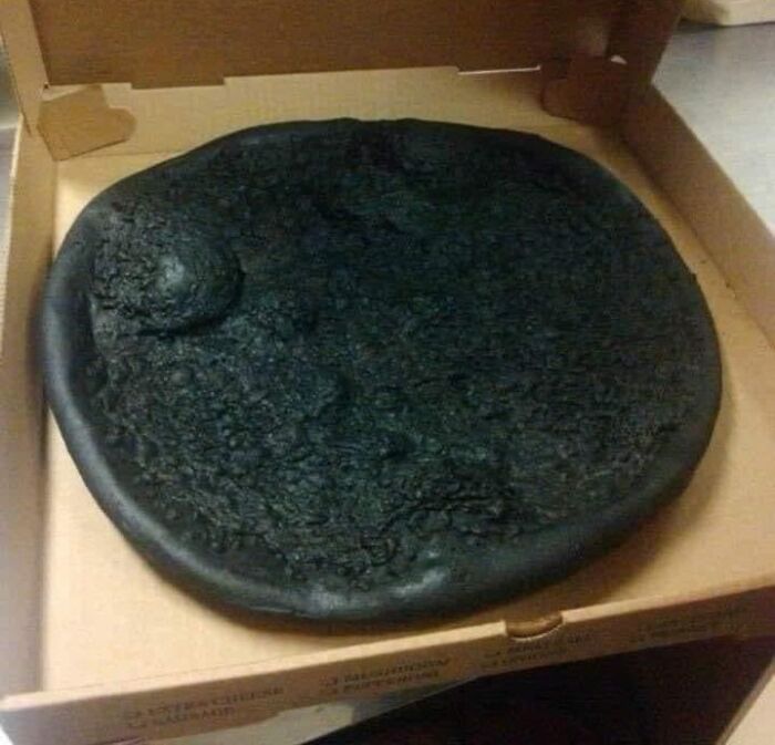 A burnt, inedible pizza in a box, representing cursed foods that might make your stomach turn.