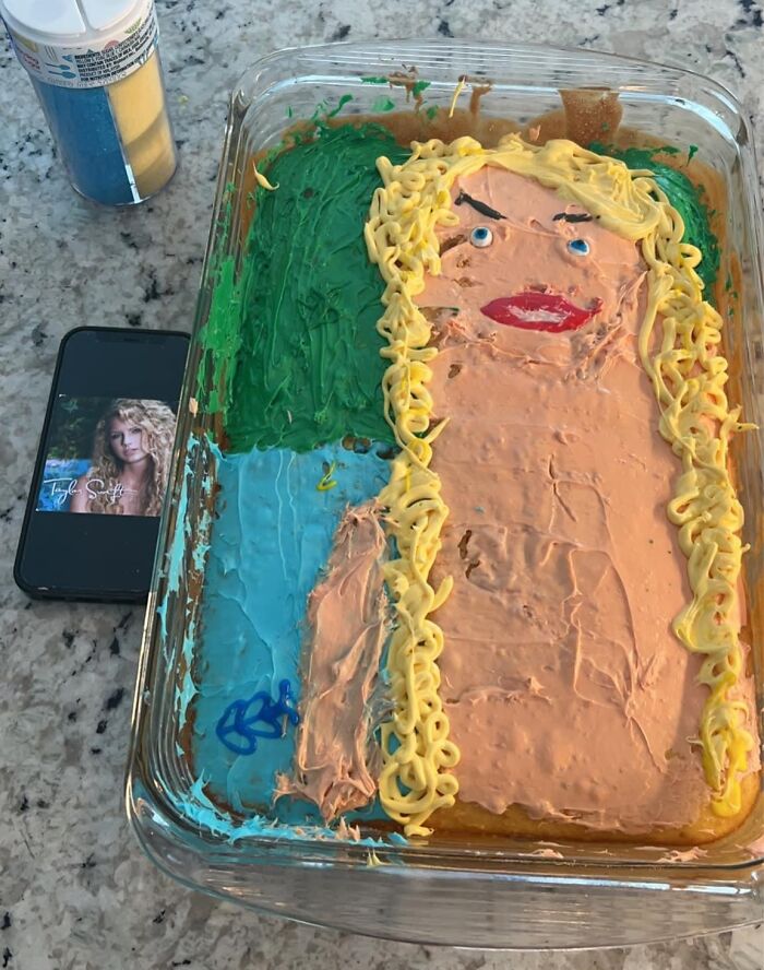 Cursed food cake with odd portrait icing on counter, phone nearby.