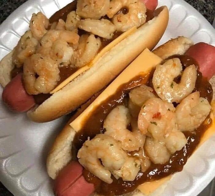 Cursed foods: hot dogs topped with shrimp, cheese, and sauce on a white plate.
