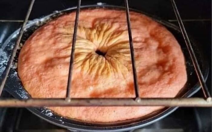 Cursed food in an oven: a strangely deformed cake with a wrinkled, sunken center.