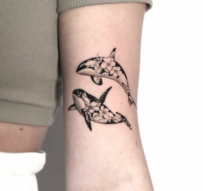 Floral orca family tattoo design on forearm, symbolizing unbreakable bonds.