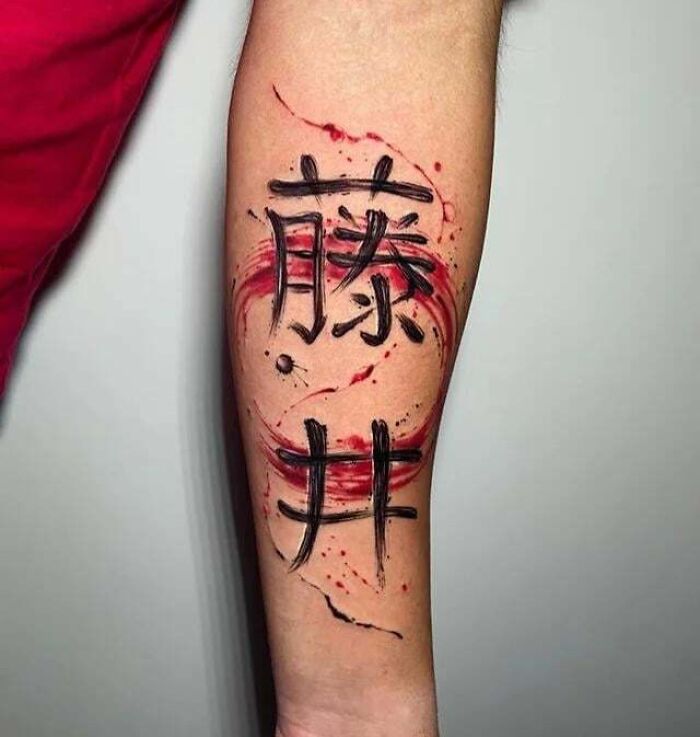 Family tattoo with bold black calligraphy and red swirls on forearm.