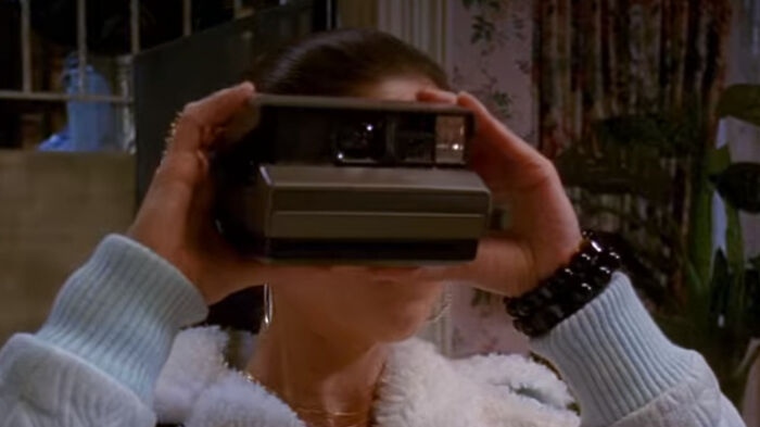 Person in a cozy outfit humorously using an old-fashioned Polaroid camera indoors.