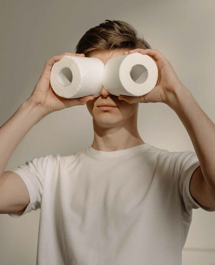 A man in a white t-shirt holding two white tissue rolls over his eyes showing unusual useless facts humor concept.