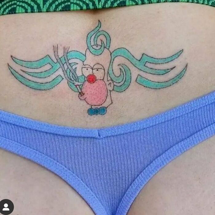 Tattoo failure on lower back illustrating a cartoon clown with colorful swirls, wearing purple clothing.