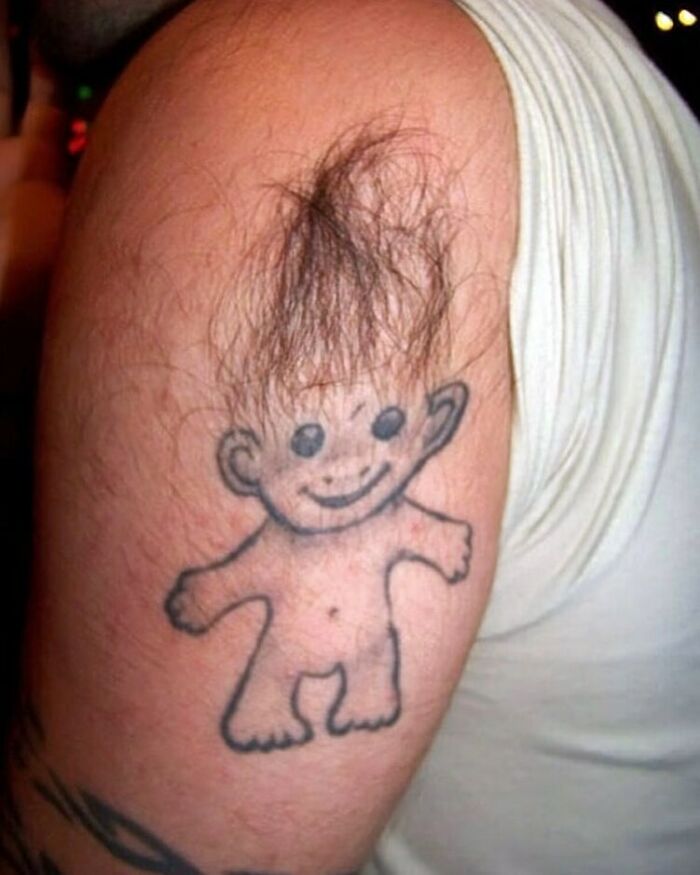 Troll doll tattoo on an arm, using arm hair as the doll’s hair, illustrating a humorous ink failure.
