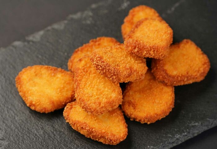 Crispy chicken nuggets arranged on a dark slate serving plate, perfect for sharing useless facts to impress friends.