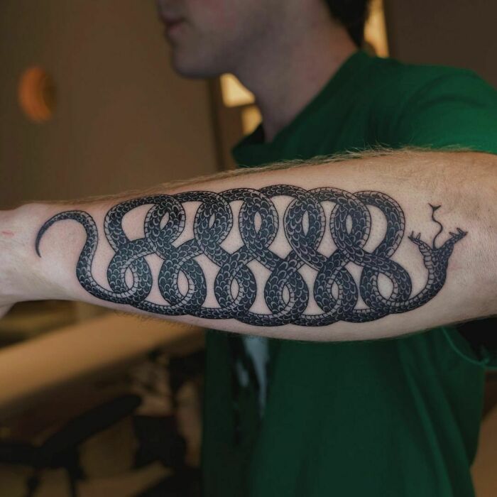 Intricate snake tattoo design on a person's forearm, showcasing detailed scales and artistic loops.