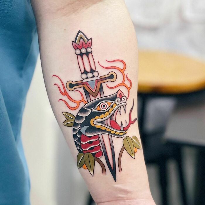 Snake tattoo with a dagger on forearm, featuring vibrant colors and intricate design.