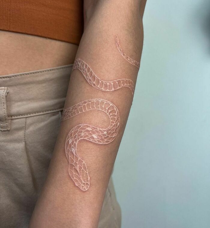 White snake tattoo on arm with detailed scales against light brown and beige background.