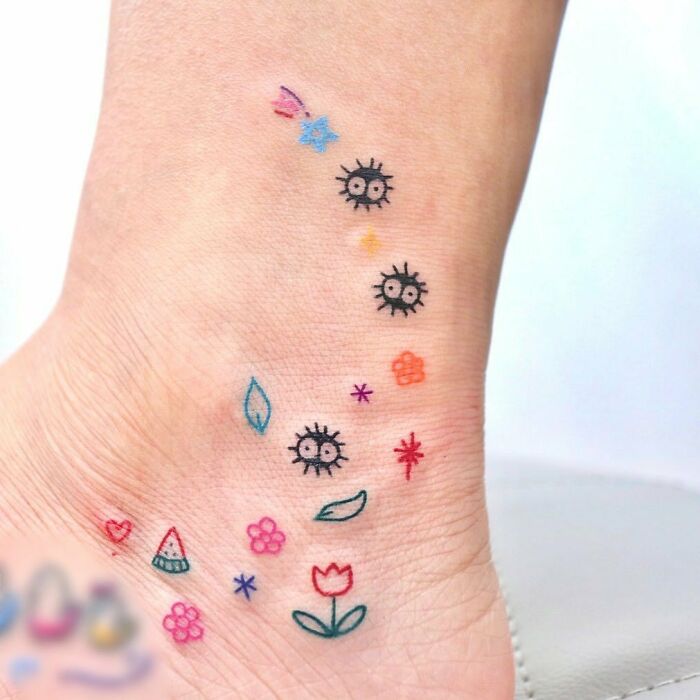 Colorful ankle tattoo with flowers and playful designs on pale skin.