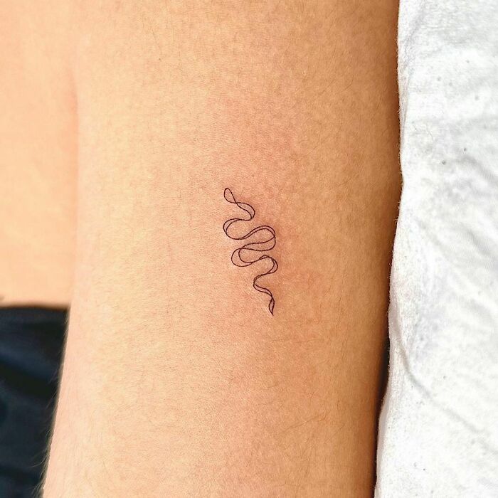 Minimalist snake tattoo design on forearm.