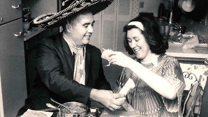 Glen Bell wearing a sombrero and sharing tacos with a woman, illustrating fun useless facts to impress friends.