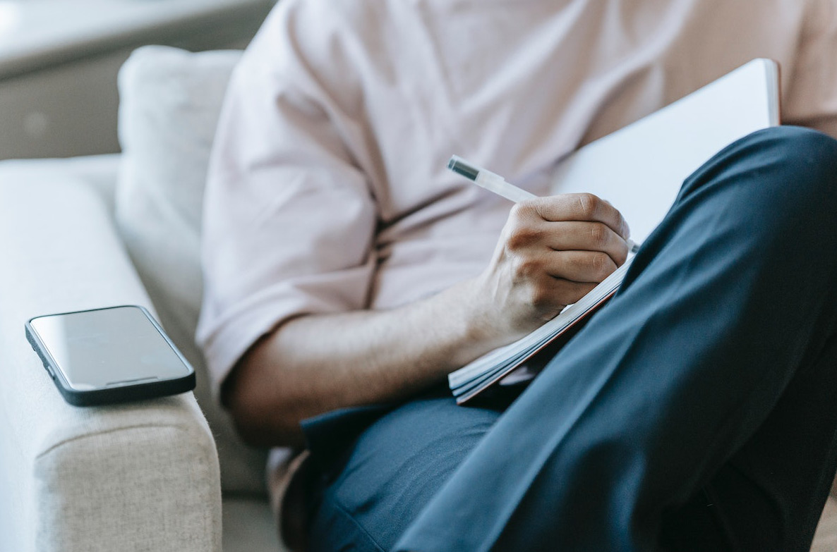 A man is writing in a notebook and sitting in an armchair