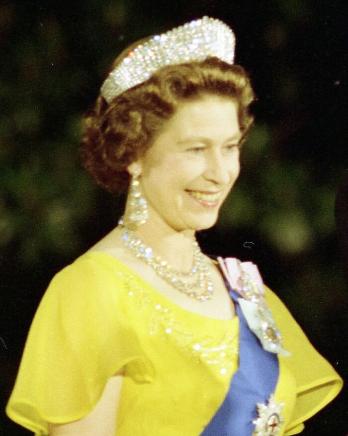Queen Elizabeth II in a yellow dress wearing a tiara and jewels, a charming image for useless facts to impress your friends.