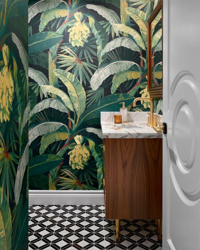 Bathroom with tropical leaves wallpaper, brown wooden vanity, marble countertop, and geometric black and white floor tiles.