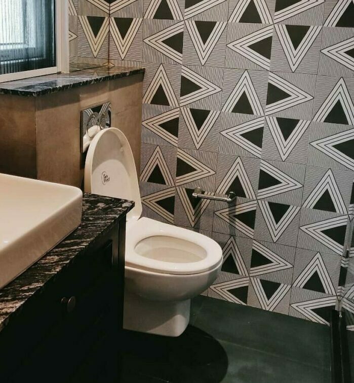 Bathroom with black geometric wallpaper, white toilet, and sink featuring a dark marble countertop in a modern space.