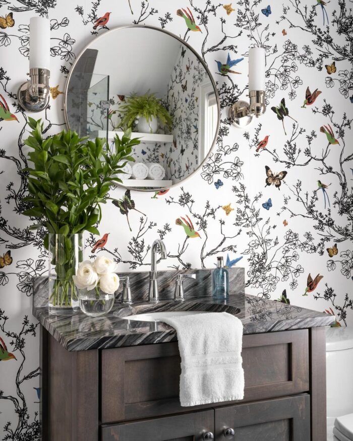 Bathroom featuring trendy wallpaper with branches, birds, and butterflies, paired with a brown cupboard and marble sink.