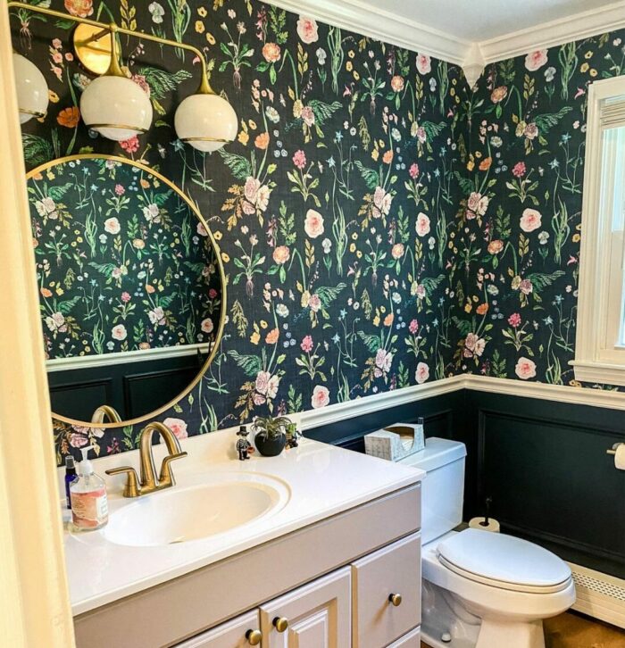 Bathroom with black floral wallpaper, gray cabinet with sink, toilet, and round mirror showcasing trendy bathroom wallpaper ideas.