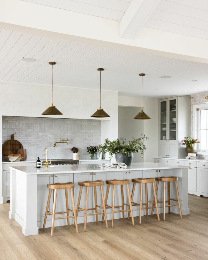 White kitchen with marble table wooden chairs and brass lights White kitchen with marble table wooden chairs and brass lights