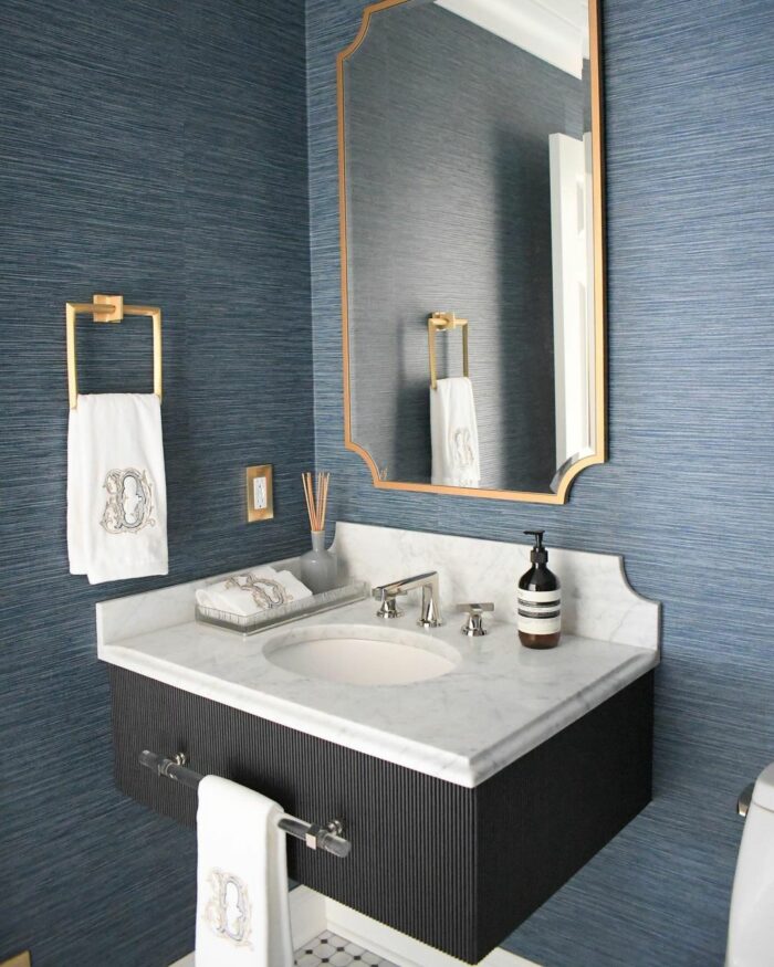 Bathroom with vinyl blue wallpaper, marble sink, gold fixtures, and matching embroidered towels in a modern space.