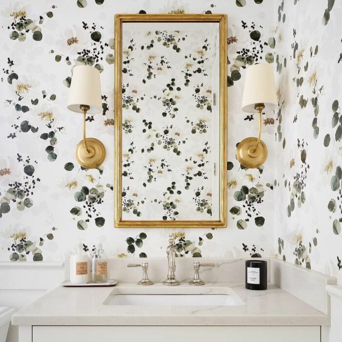 Bathroom with minimalist floral wallpaper, marble sink, gold-framed mirror, and brass wall sconces showcasing trendy bathroom wallpaper ideas.