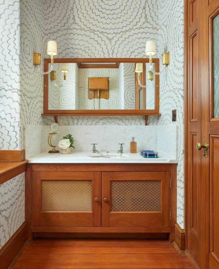Bathroom with mid-century modern striped wallpaper and wooden vanity featuring a white marble countertop and sink.