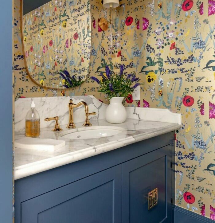 Bathroom with colorful flower wallpaper and blue cupboard featuring a marble sink and gold fixtures, showcasing trendy bathroom wallpaper ideas.