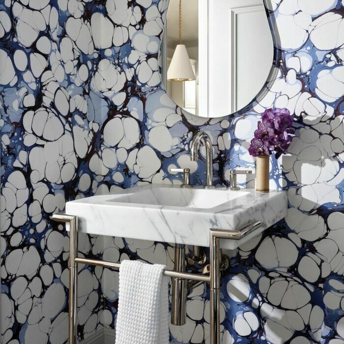 Bathroom with trendy blue cloud wallpaper and a marble sink featuring modern fixtures and a small mirror.