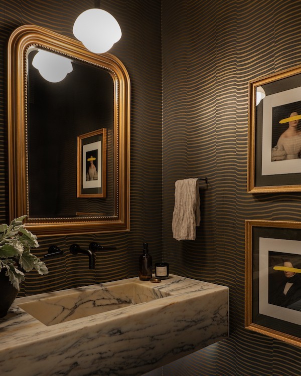 Bathroom with dark striped trendy wallpaper and a marble sink, featuring gold-framed mirror and framed artwork on walls.