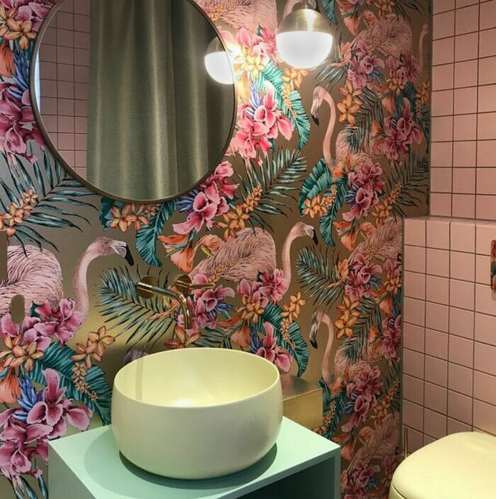 Bathroom with bright flower and flamingo wallpaper, round mirror, modern sink, and soft lighting fixtures.