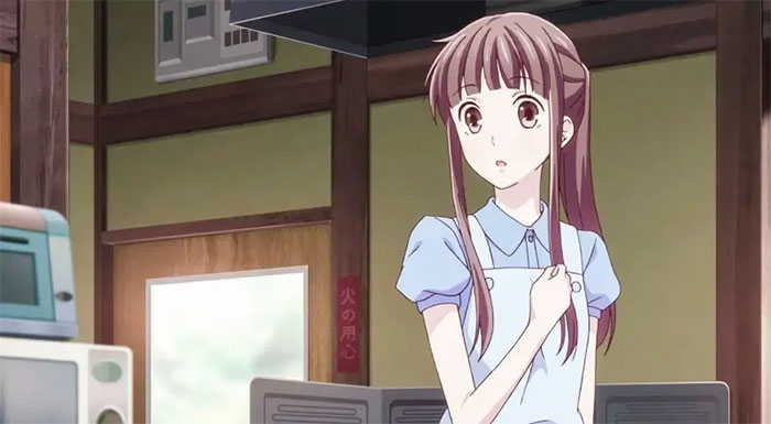 Anime girl in a blue shirt looks surprised, standing in a traditional Japanese interior.