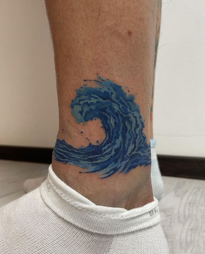 Blue wave ankle tattoo design on leg with white sock, showcasing tattoo care and inspirations.