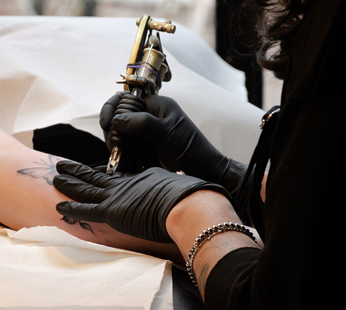 Tattoo artist in gloves applying a design on a person's arm in a studio setting.