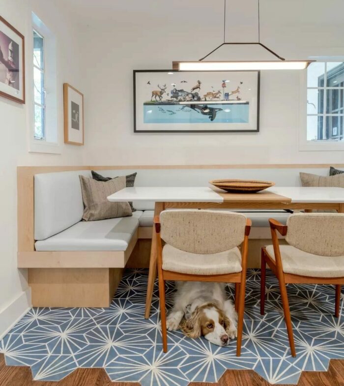 Wooden banquette seating with white table chairs and a dog resting on a blue geometric patterned rug beneath the table.