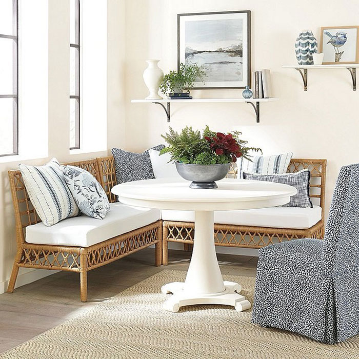 Rattan banquette seating with patterned pillows and white round table in a bright dining nook setting