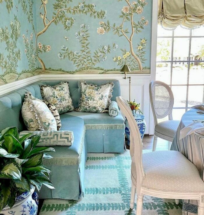 Blue banquette seating with floral cushions and nature-inspired wallpaper in a cozy dining nook with natural light.