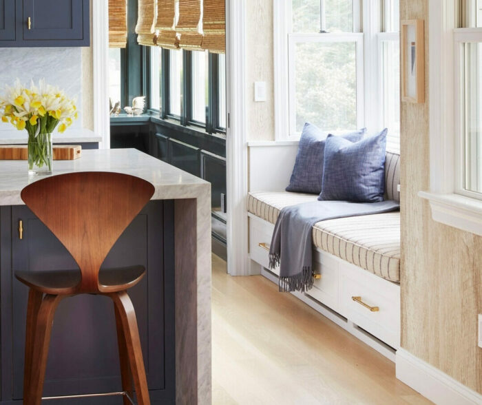 White window banquette seating with blue pillows and striped cushion in a bright kitchen corner.