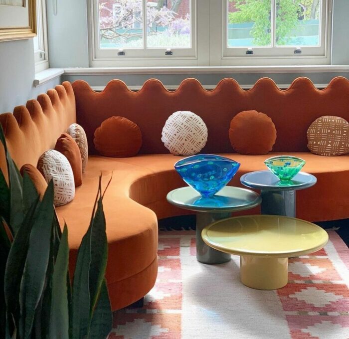 Curvy orange banquette seating with decorative pillows and small modern tables in a bright living space.