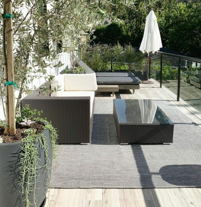 Black banquette seating with white pillows on a sunny patio, surrounded by greenery and modern outdoor decor.