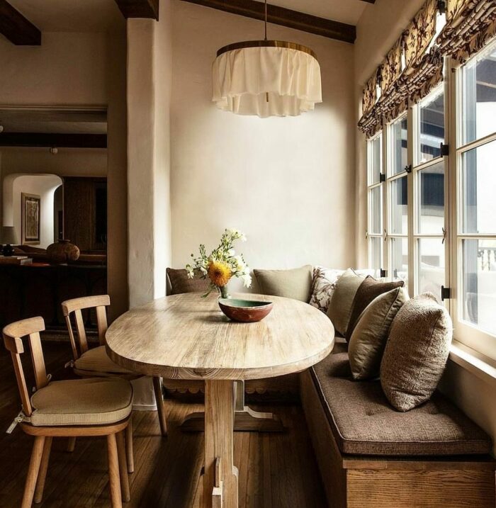 Wooden banquette seating near window with cushions, paired with a rustic wooden table and chairs in a cozy dining nook.