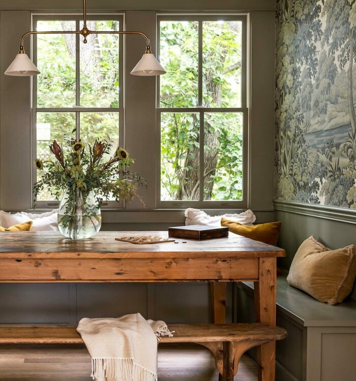 Gray banquette seating with nature-inspired wallpaper and rustic wooden table in a cozy dining nook setting