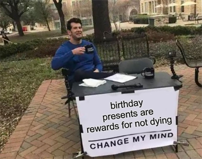 Man with a sign that reads "birthday presents are rewards for not dying" in a humorous meme setting.