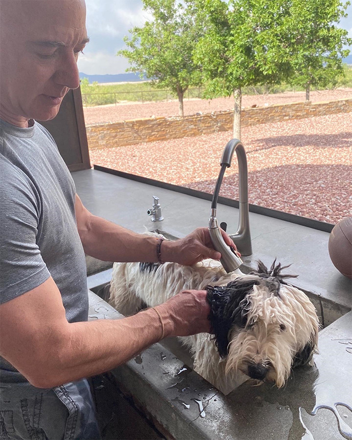 Man with muscular arms washing a dog in an outdoor sink, showcasing buff celeb fitness and lifestyle.