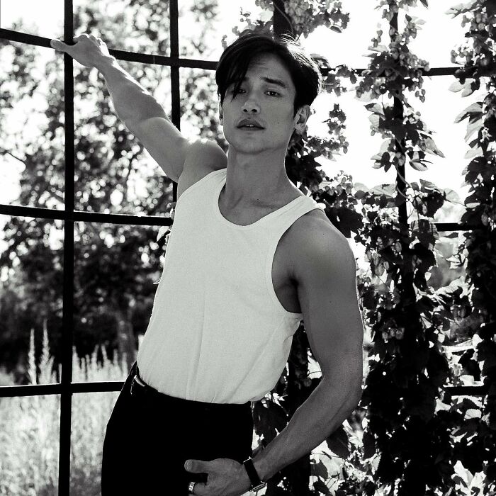 Asian male celebrity posing outdoors showing off his muscular and buff arms in a sleeveless white shirt.